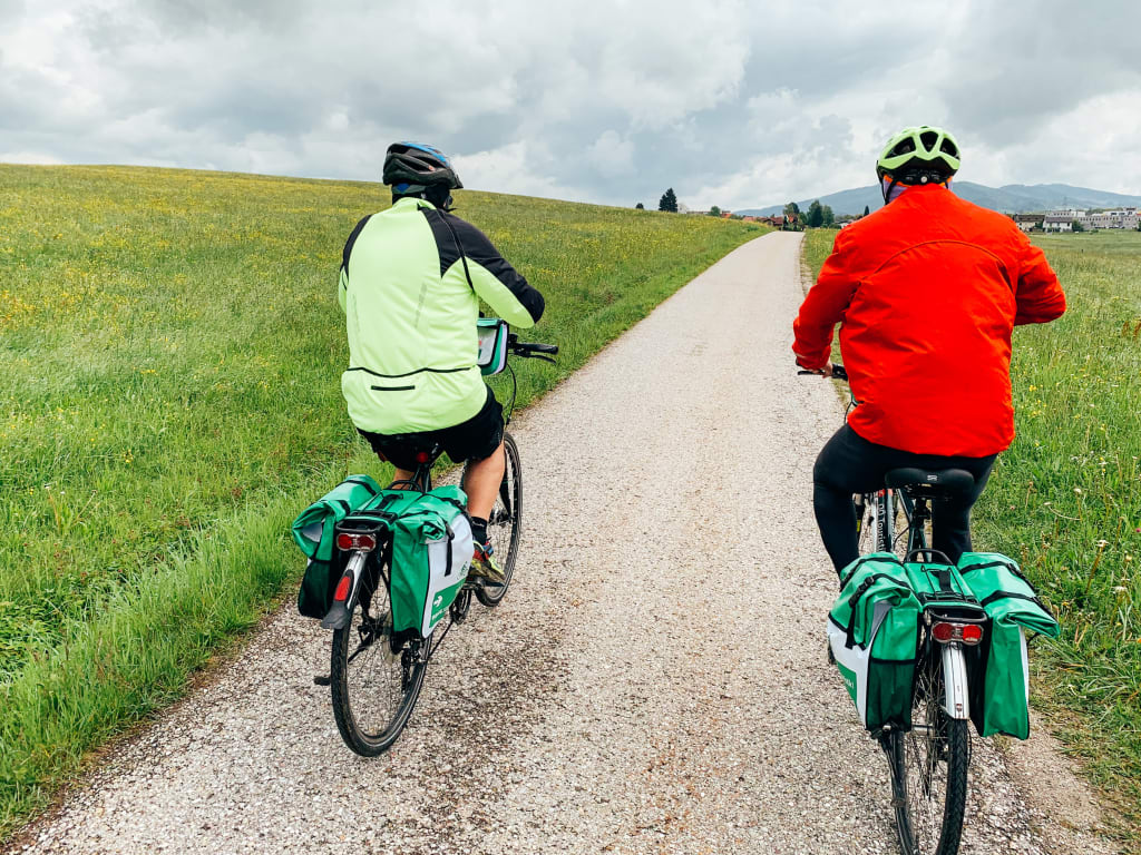 Coppia in bicicletta lungo un percorso verdeggiante con montagne sullo sfondo vicino a Bad Goisern.